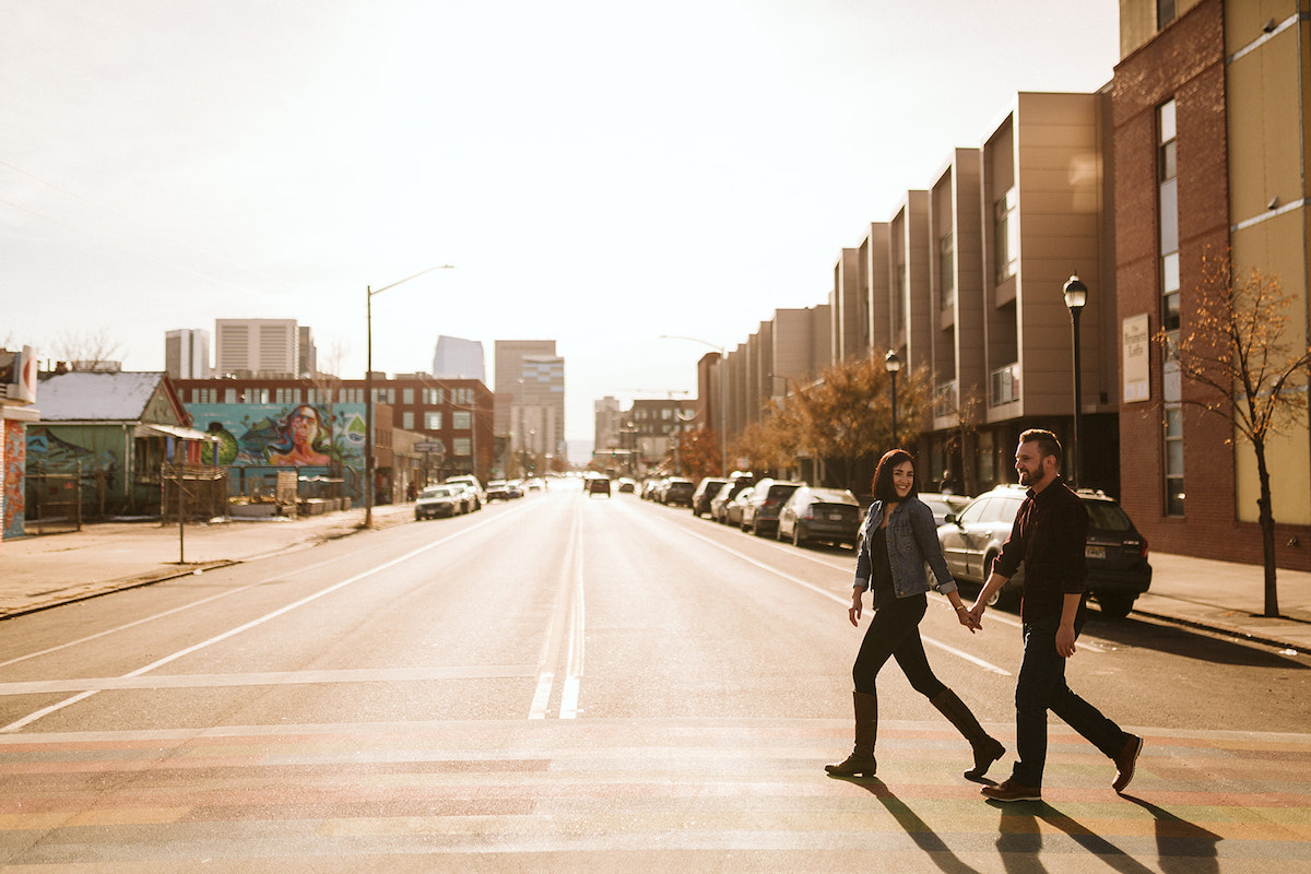 man and woman holding hands crossing the street on a sunny day