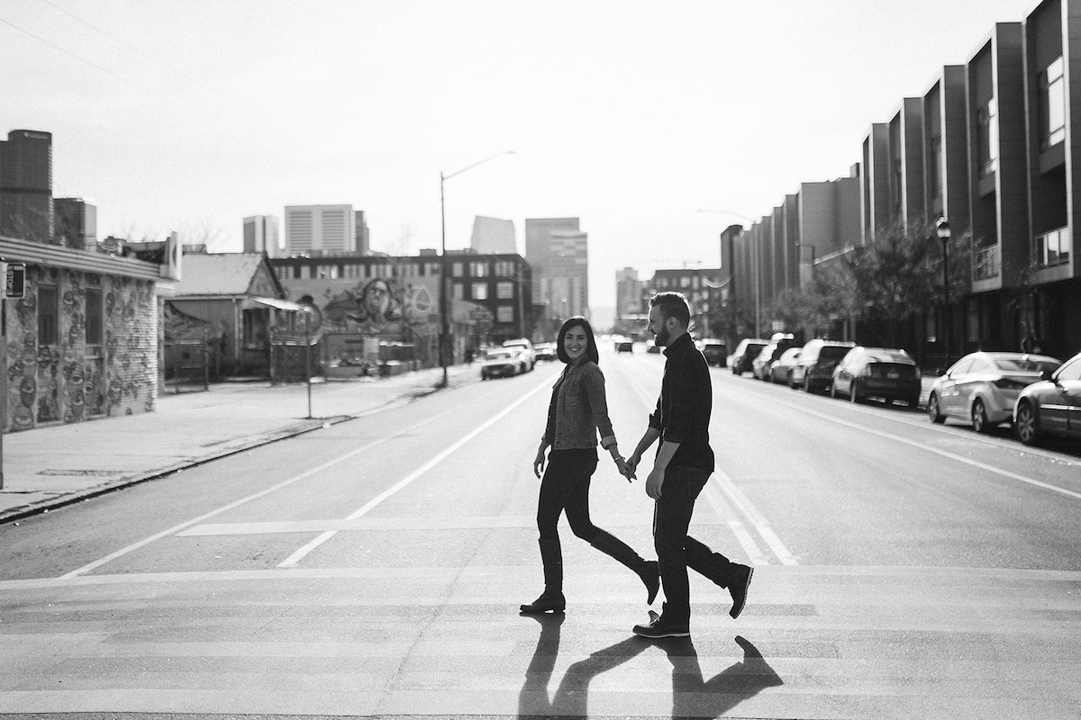 man and woman holding hands crossing the street on a sunny day