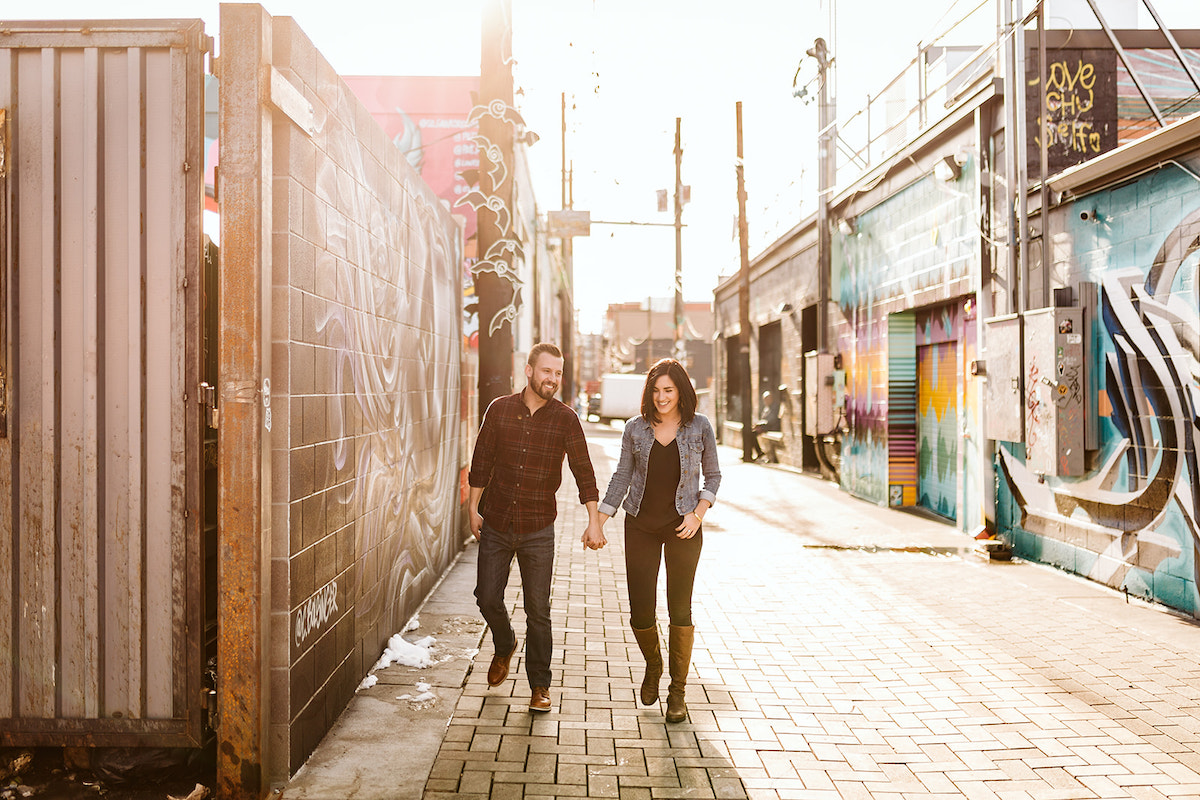 man and woman holding hands walking on a bricked alleyway between colorfully painted buildings in Denver's RiNo District