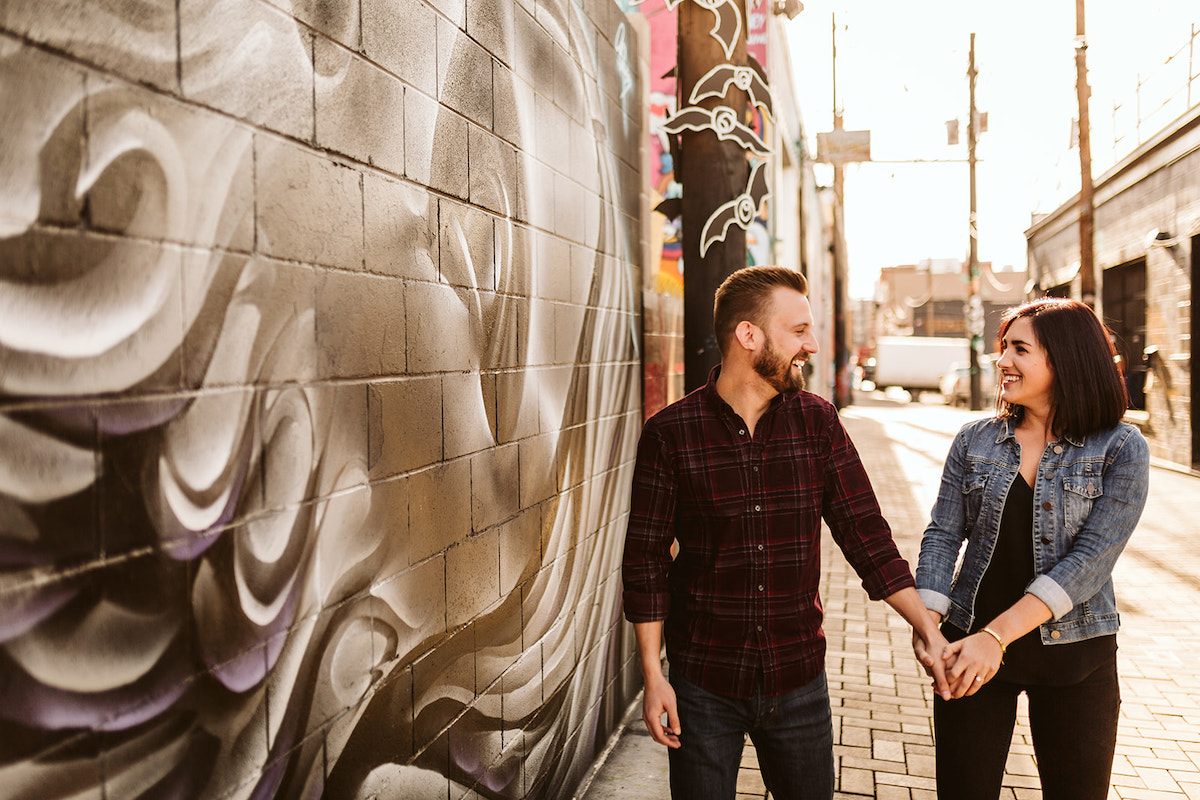 man and woman holding hands walking on a bricked alleyway between colorfully painted buildings in Denver's RiNo District