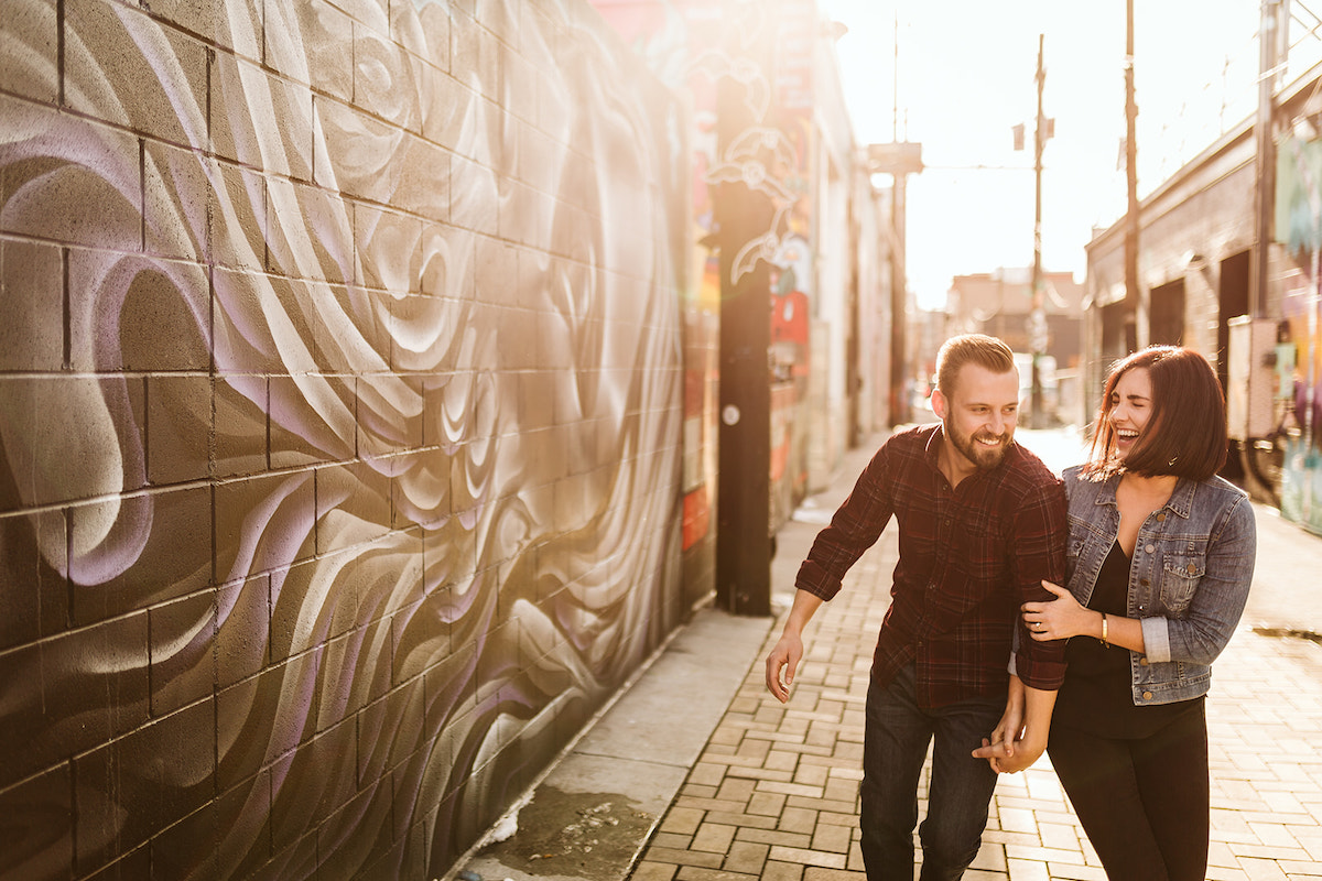 man and woman holding hands and laughing on a bricked alleyway between colorfully painted buildings in Denver's RiNo District