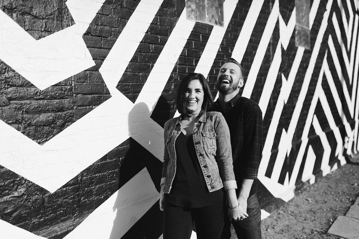 man and woman stand in front of boldly painted brick wall for their Denver RiNo engagement photos