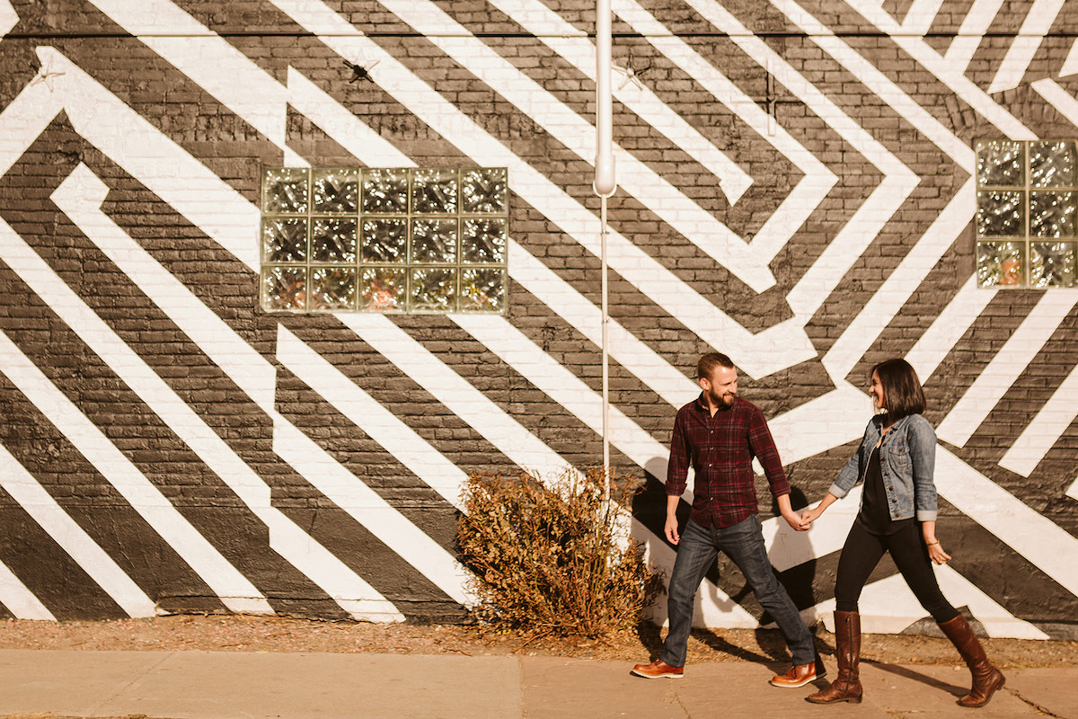 man and woman hold hands and walk in front of boldly painted black and white brick wall in Denver's RiNo art district