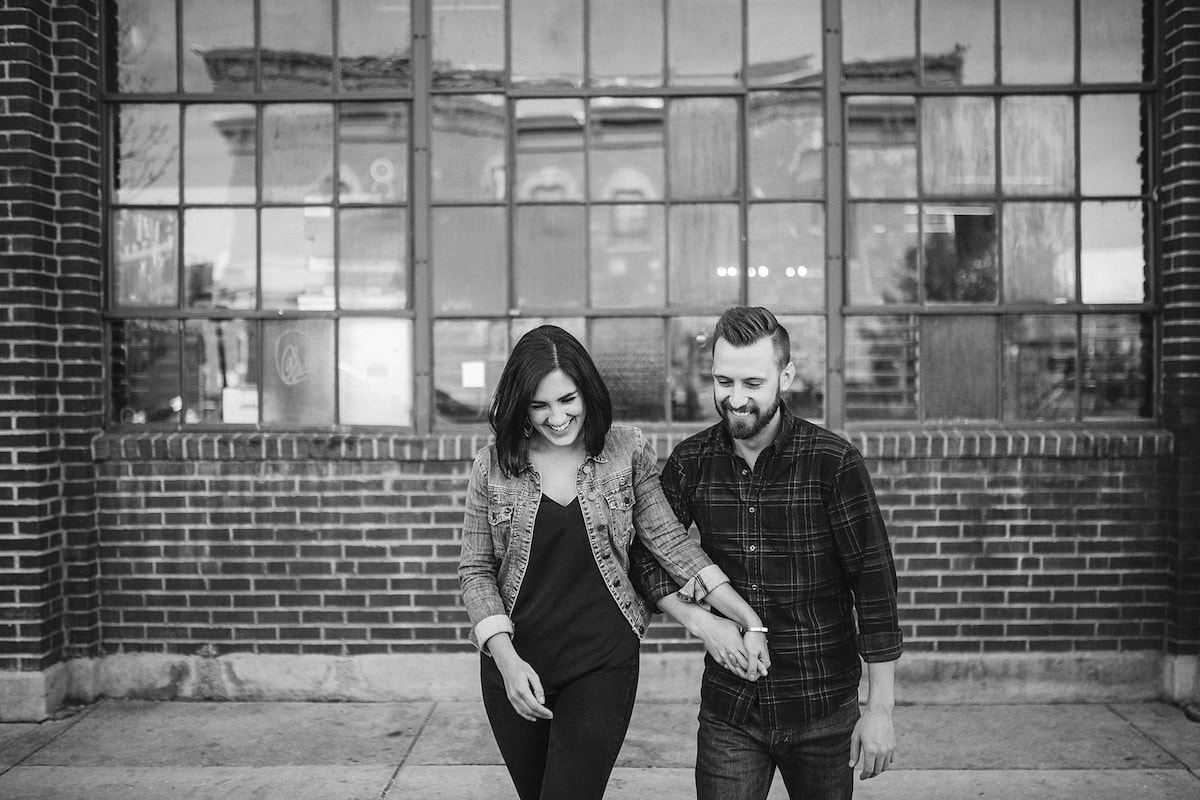 man and woman holding hands and walking away from tall metal-framed windows and brick building in Denver's RiNo district