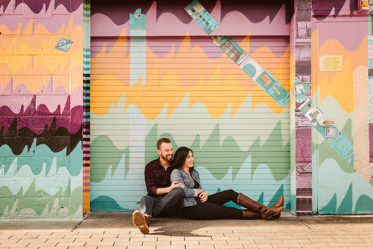 man and woman sit against a painted wall in Denver's RiNo art district for engagement photos