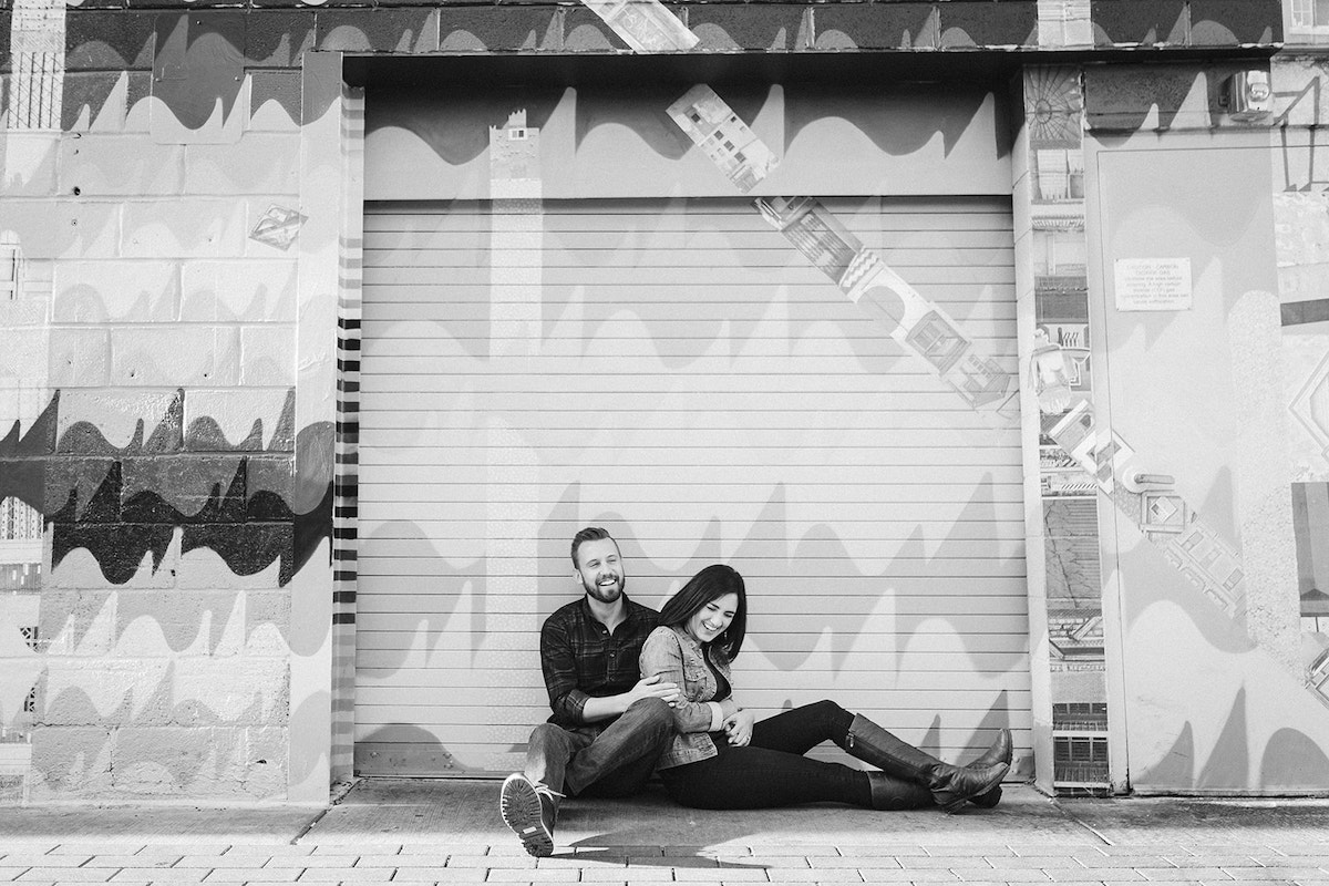 man and woman sit on the ground leaning against a brightly painted wall for Denver RiNo district engagement photos
