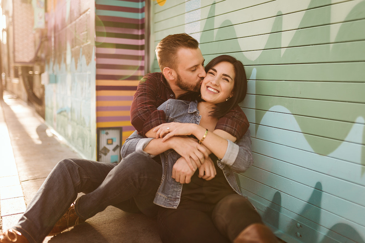 man and woman sit on the ground leaning against a brightly painted wall for Denver RiNo district engagement photos