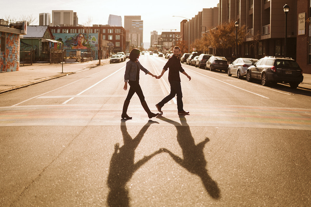 man and woman holding hands crossing the street on a sunny day
