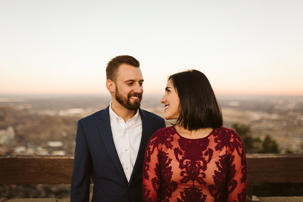 Man in dark blue suit and woman in long maroon dress look at each other and smile.