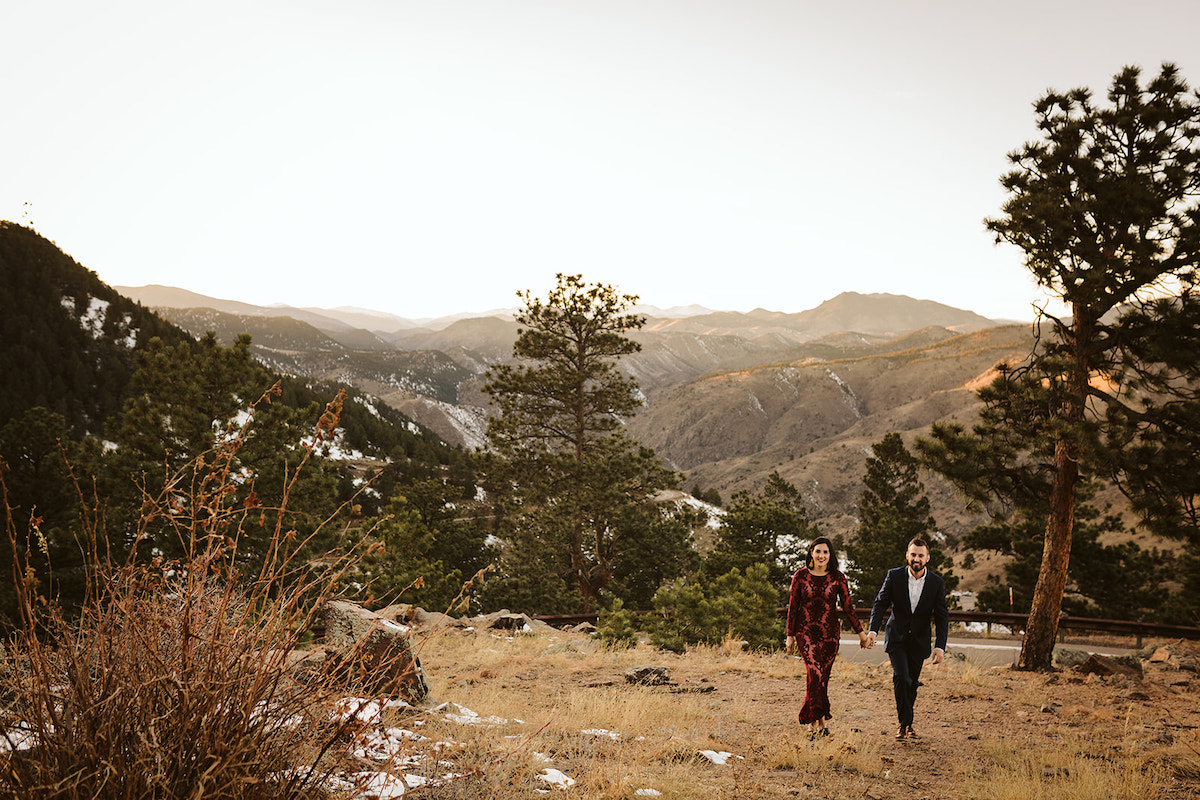 Man in dark suit and woman in maroon dress in a grassy field for engagement photos on Colorado's Lookout Mountain
