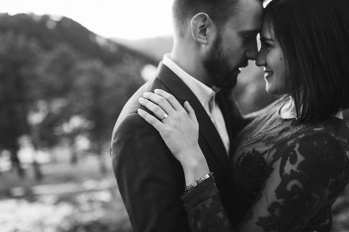 Man in dark suit and woman in maroon dress press foreheads together in front of Colorado mountain scene