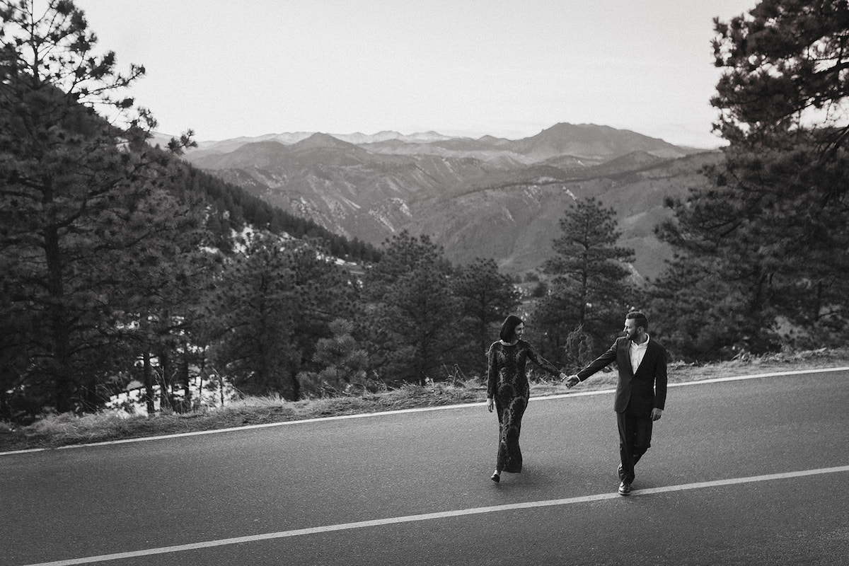 Man and woman hold hands and cross the street overlooking the mountain view from Lookout Mountain in Colorado