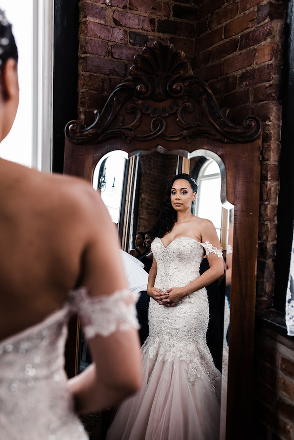 bride looks at herself in her mermaid cut wedding dress an ornately carved mirror