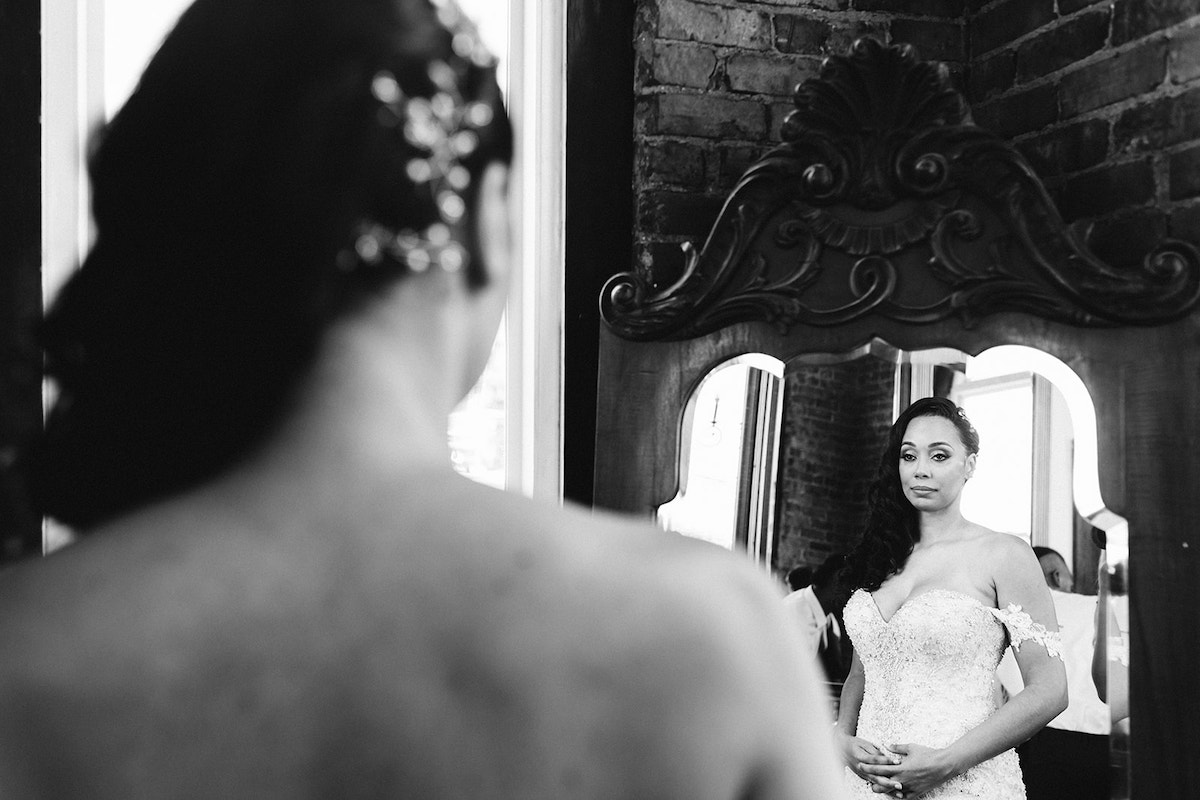 bride looks at herself in an ornately carved mirror