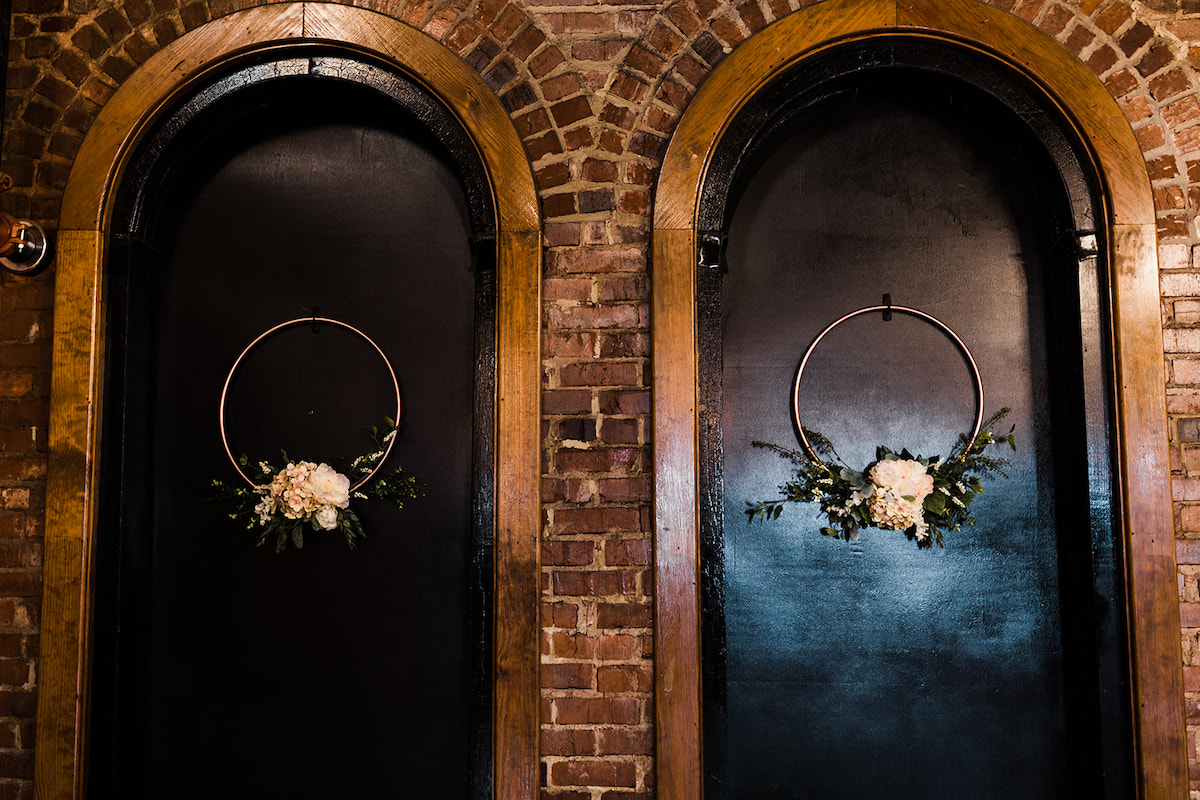 simple metal wreaths with small flower display at the bottom hang against painted black arched windows
