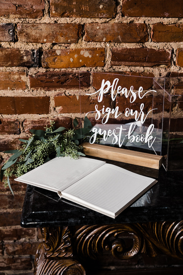 guestbook and sign sit on an ornate table next to a brick wall