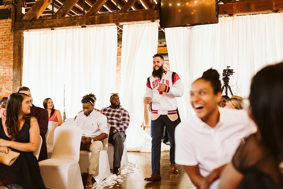 groom wears a Chicago Bulls basketball jacket over his suit coat as he walks the aisle at The Church on Main in Chattanooga