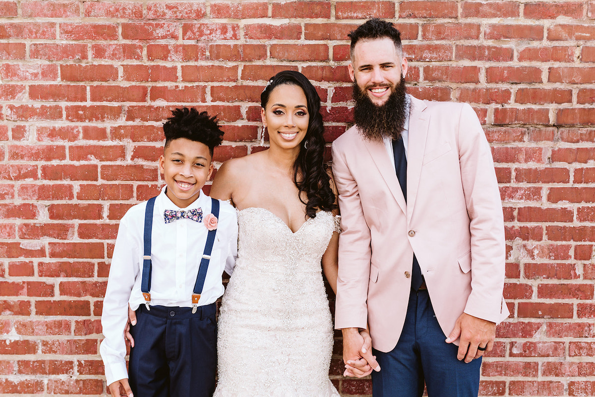 groom and bride and her son hold hands in front of a brick wall outside The Church on Main in Chattanooga, TN