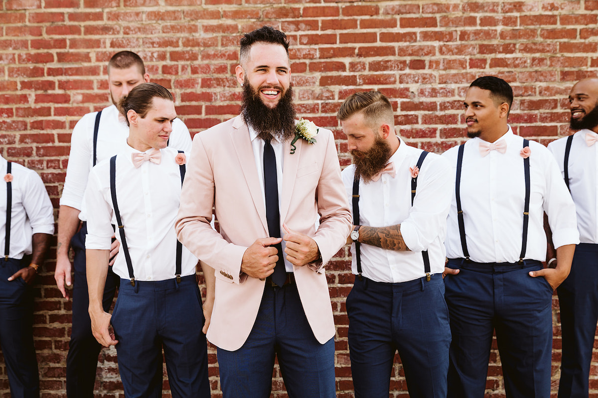 Groom and groomsmen laugh in front of a tall brick wall after his Church on Main wedding