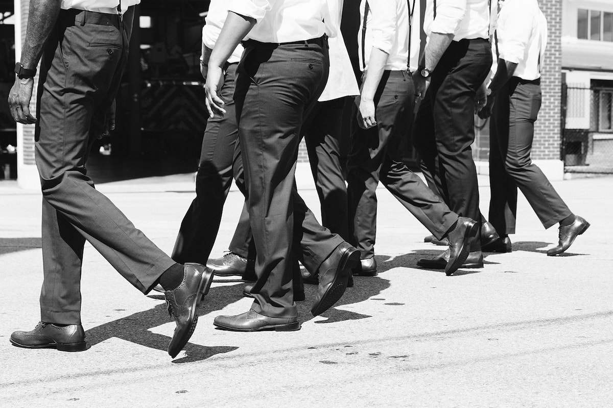 groomsmen in dark pants and white shirts walk together down the middle of the road