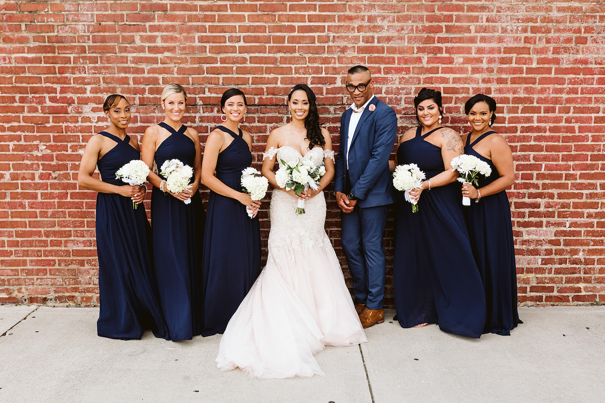 bride and bridal party stand in front of a tall brick wall after her Church on Main wedding in Chattanooga, TN