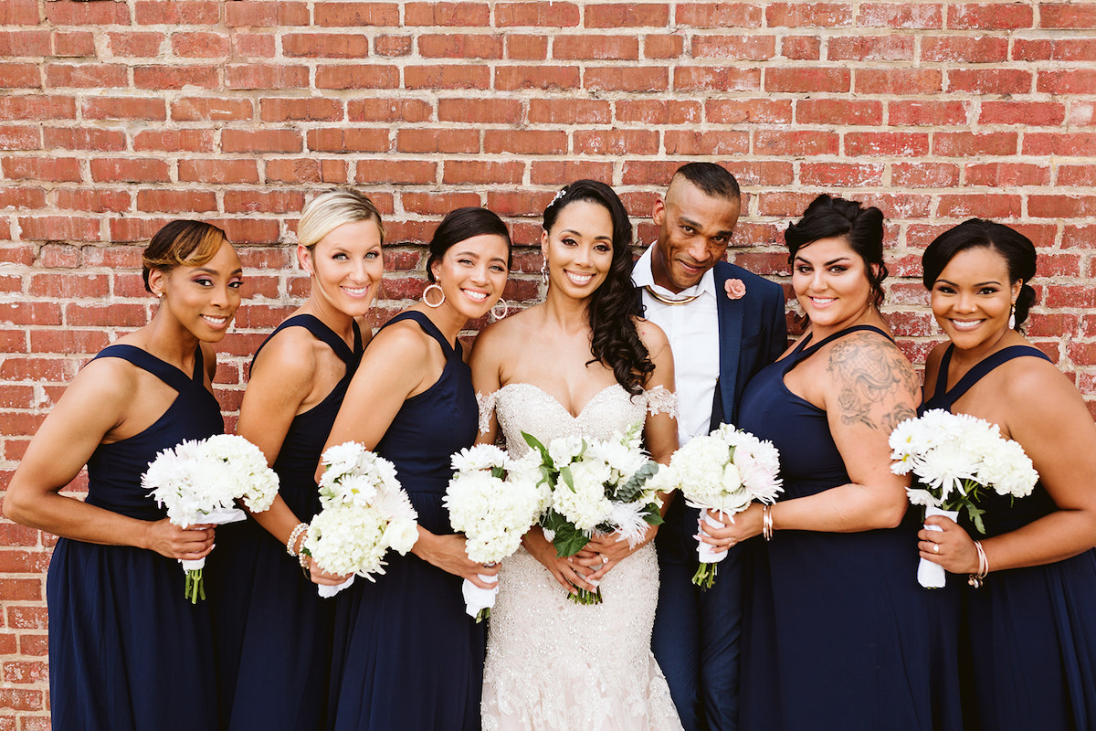 bride and bridal party stand in front of a tall brick wall after her Church on Main wedding in Chattanooga, TN