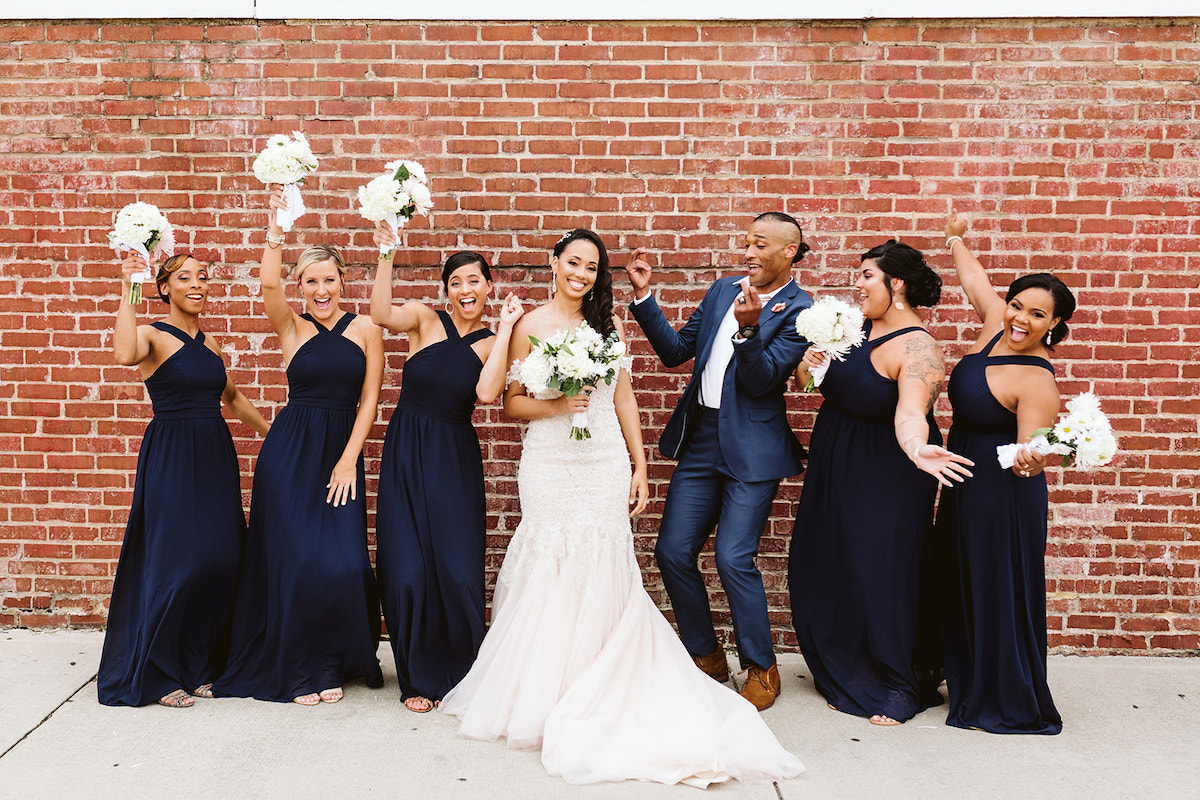 bride and bridal party stand in front of a tall brick wall after her Church on Main wedding in Chattanooga, TN