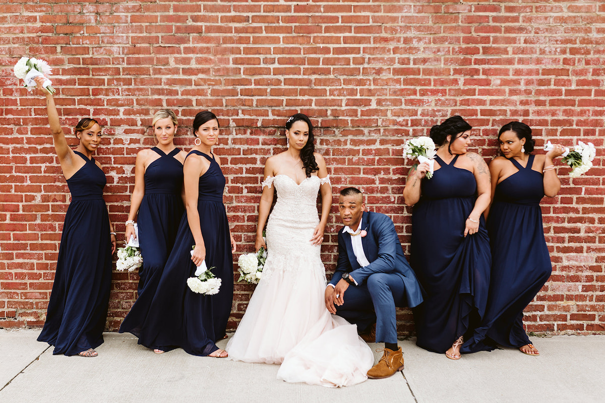 bride and bridal party stand in front of a tall brick wall after her Church on Main wedding in Chattanooga, TN
