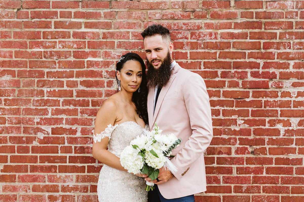 Bride and groom stand close to each other in front of a brick wall