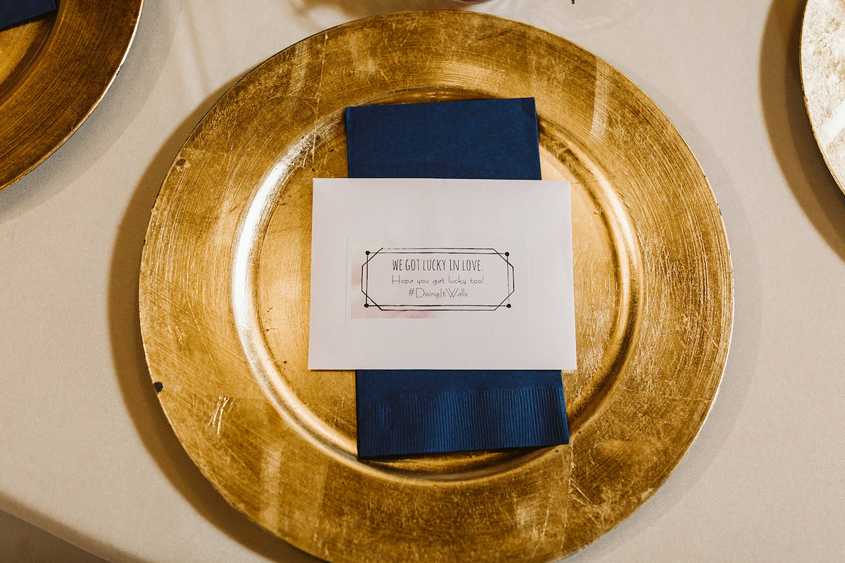 White card sits on a deep blue napkin on tope of a gold charger plate.