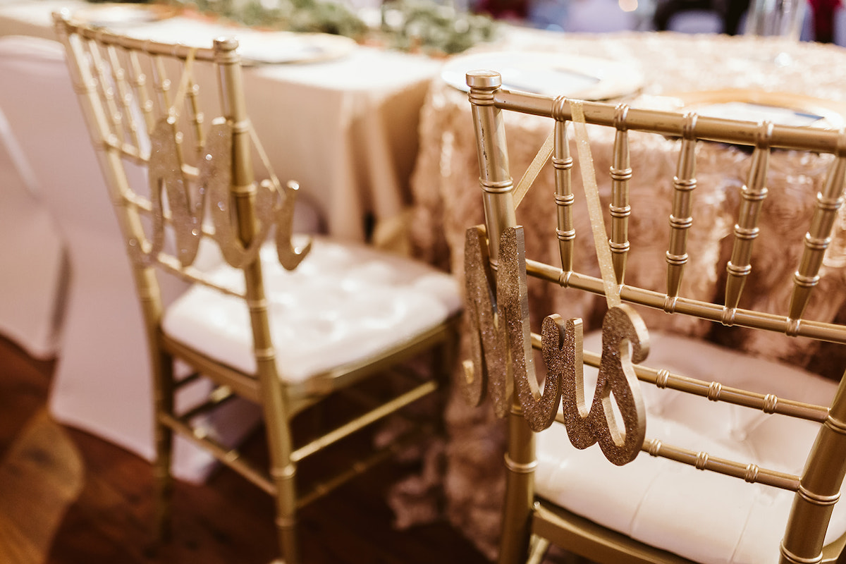 Gold, glittered Mr and Mrs signs hang on the corner of gold cane chairs