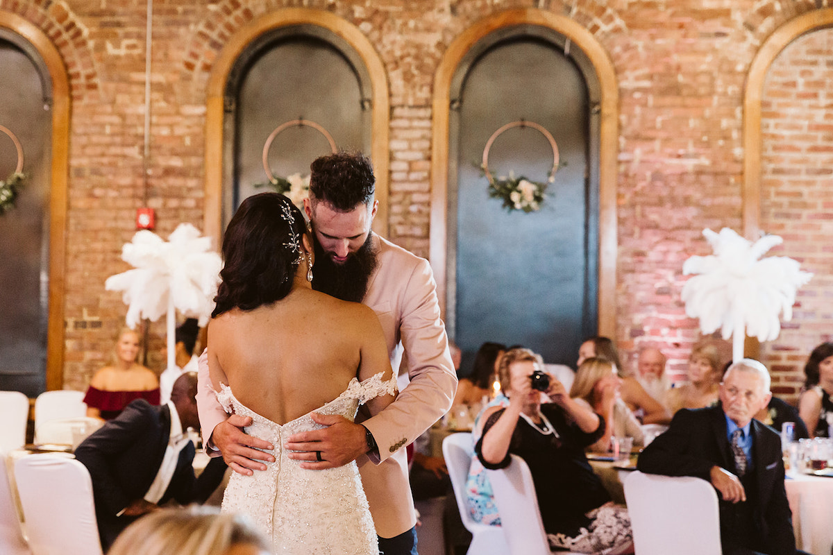 bride smiles at groom as they dance with the tall, arched windows the The Church on Main behind them. Wedding guests watch them dance.