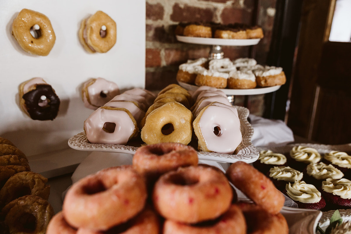 multiple flavors of donuts stacked on various plates. more donuts hang on dowels on a wall.