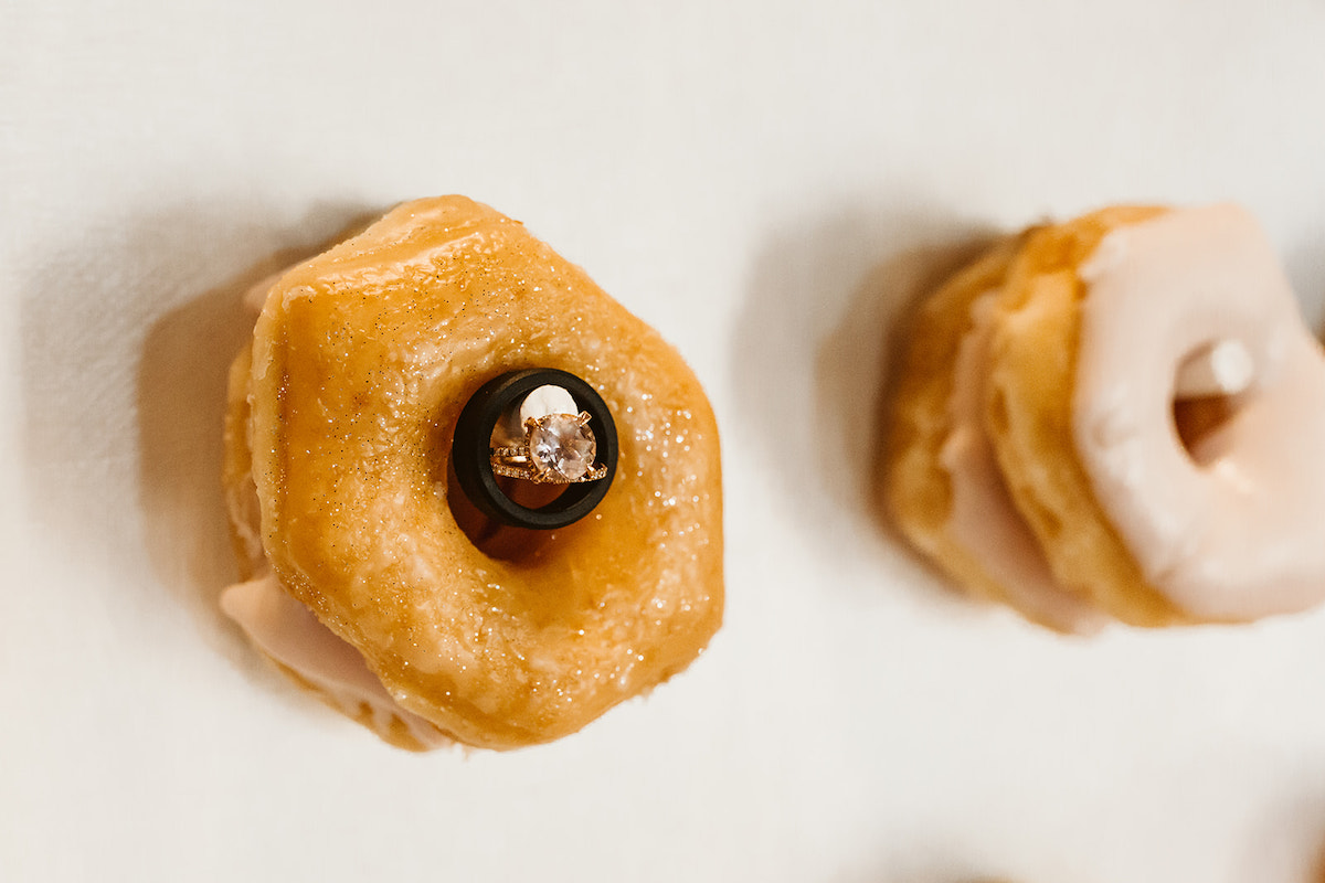 diamond ring and black wedding band hang inside the hole of a donut