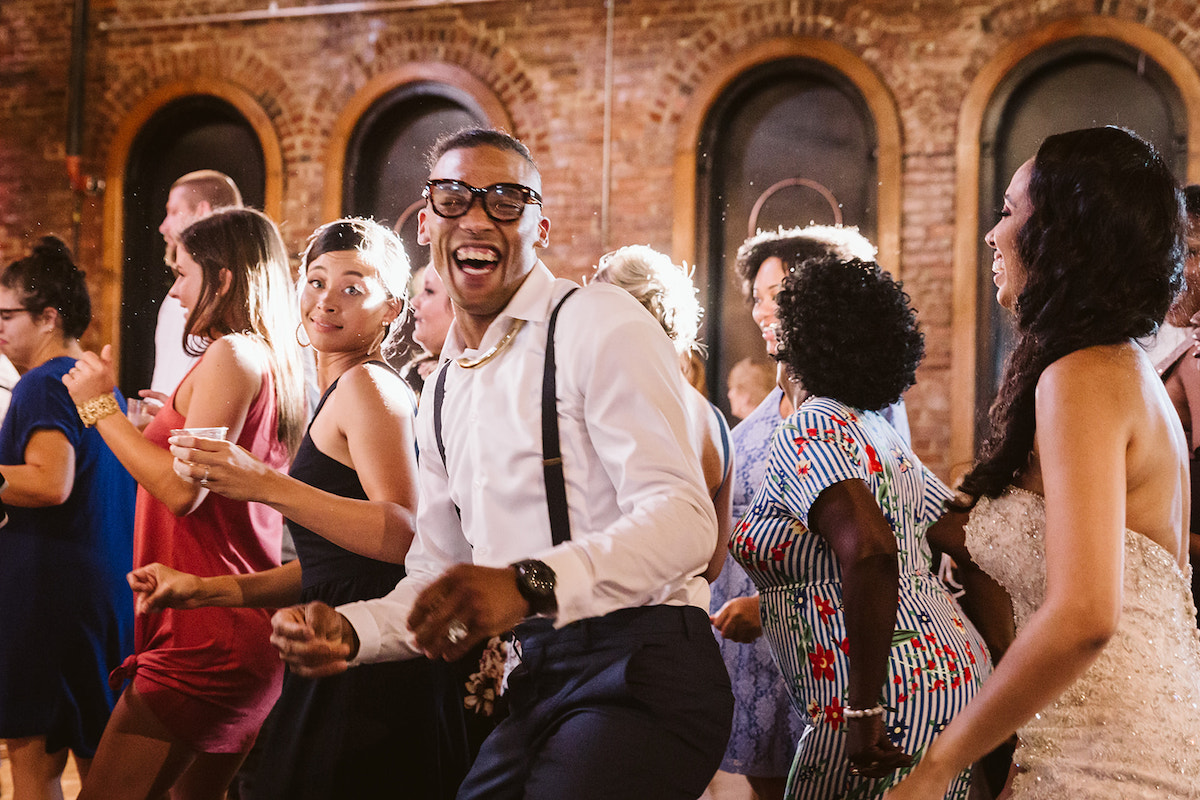 Bride dances and laughs with friends as the tall, arched windows at The Church on Main frame them.