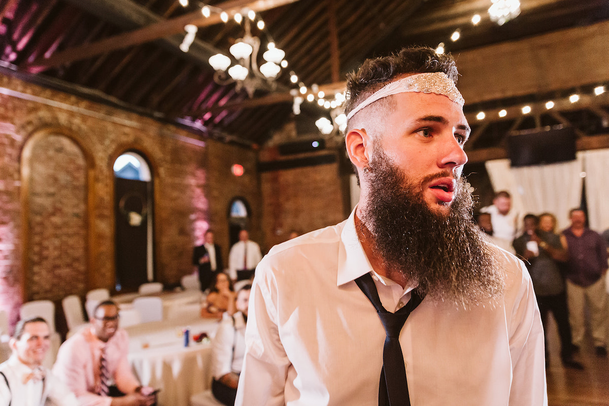 groom wears bride's white lacy garter around his head under open rafters of The Church on Main in Chattanooga