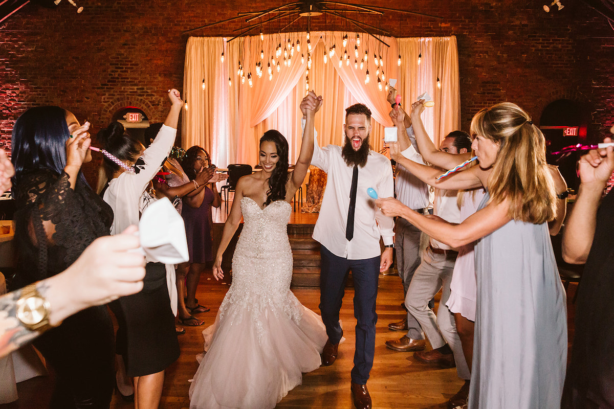 Bride and groom hold hands in the air and walk between two rows of cheering friends