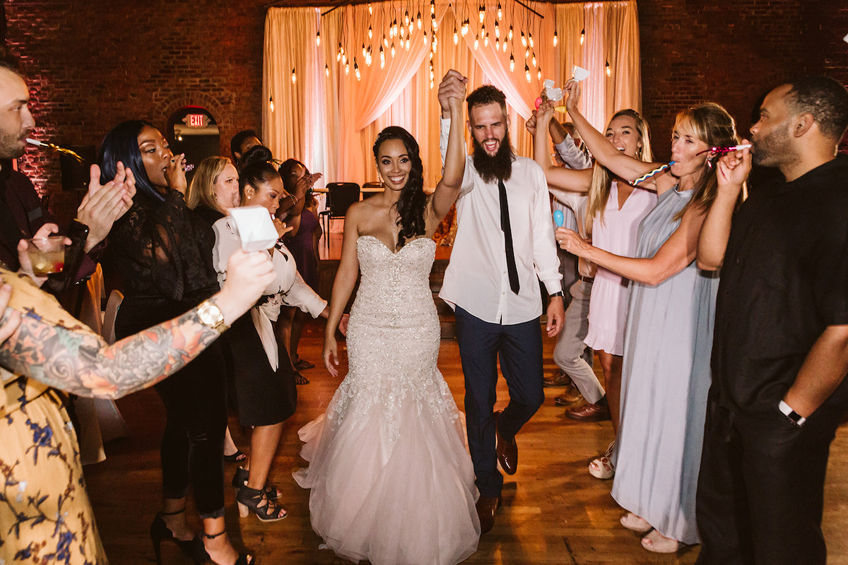 Bride and groom hold hands in the air and walk between two rows of cheering friends