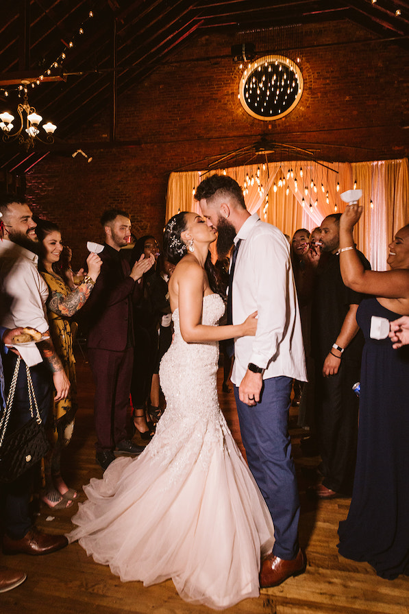 Bride and groom kiss while guests clap and ring white bells around them