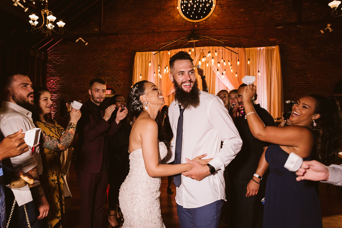 Bride and groom smile at each other while guests clap and ring white bells around them