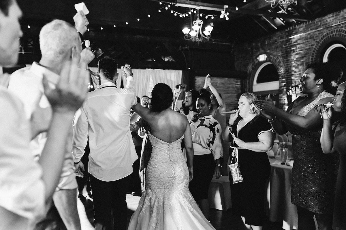 Bride and groom hold hands in the air and walk between two rows of cheering friends