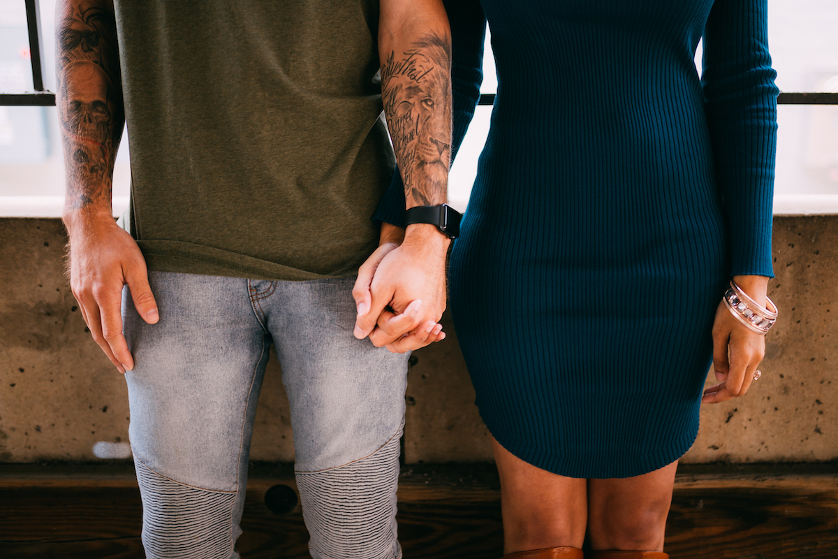 man in slim jeans and green t-shirt holds hand with woman in long-sleeve, emerald jewel tone dress