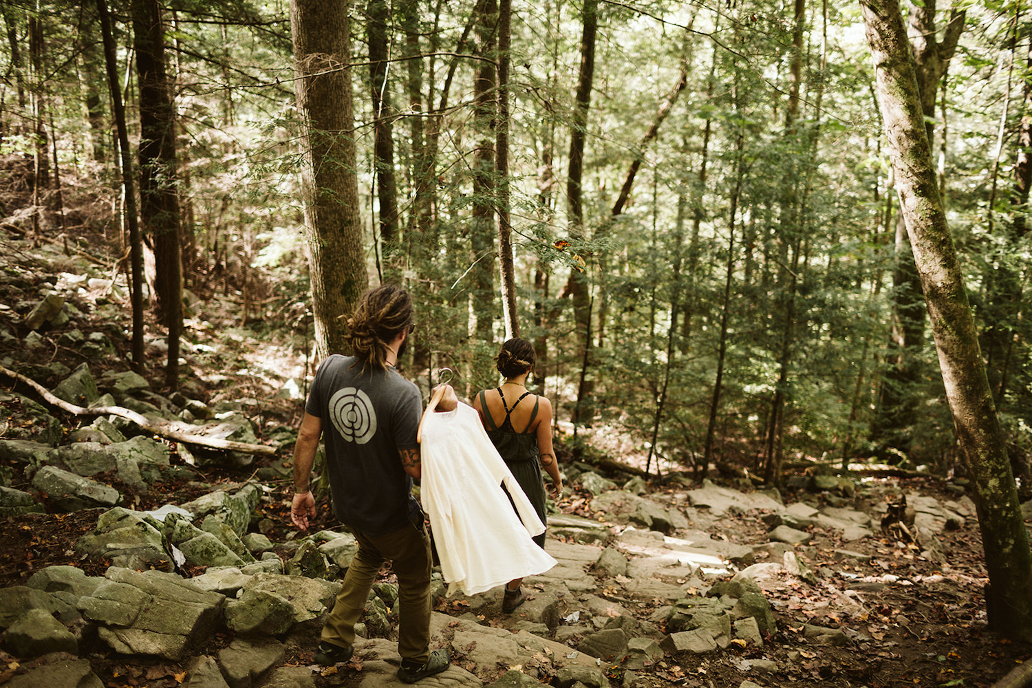 man carries white shirt as he hikes down rock steps to Foster Falls behind woman