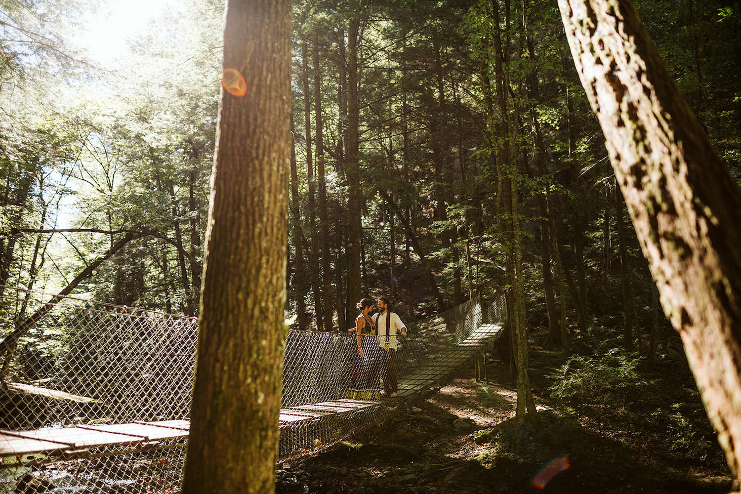 man and woman stand on wooden suspension bridge at Foster Falls in Chattanooga for their bohemian festival wedding portraits