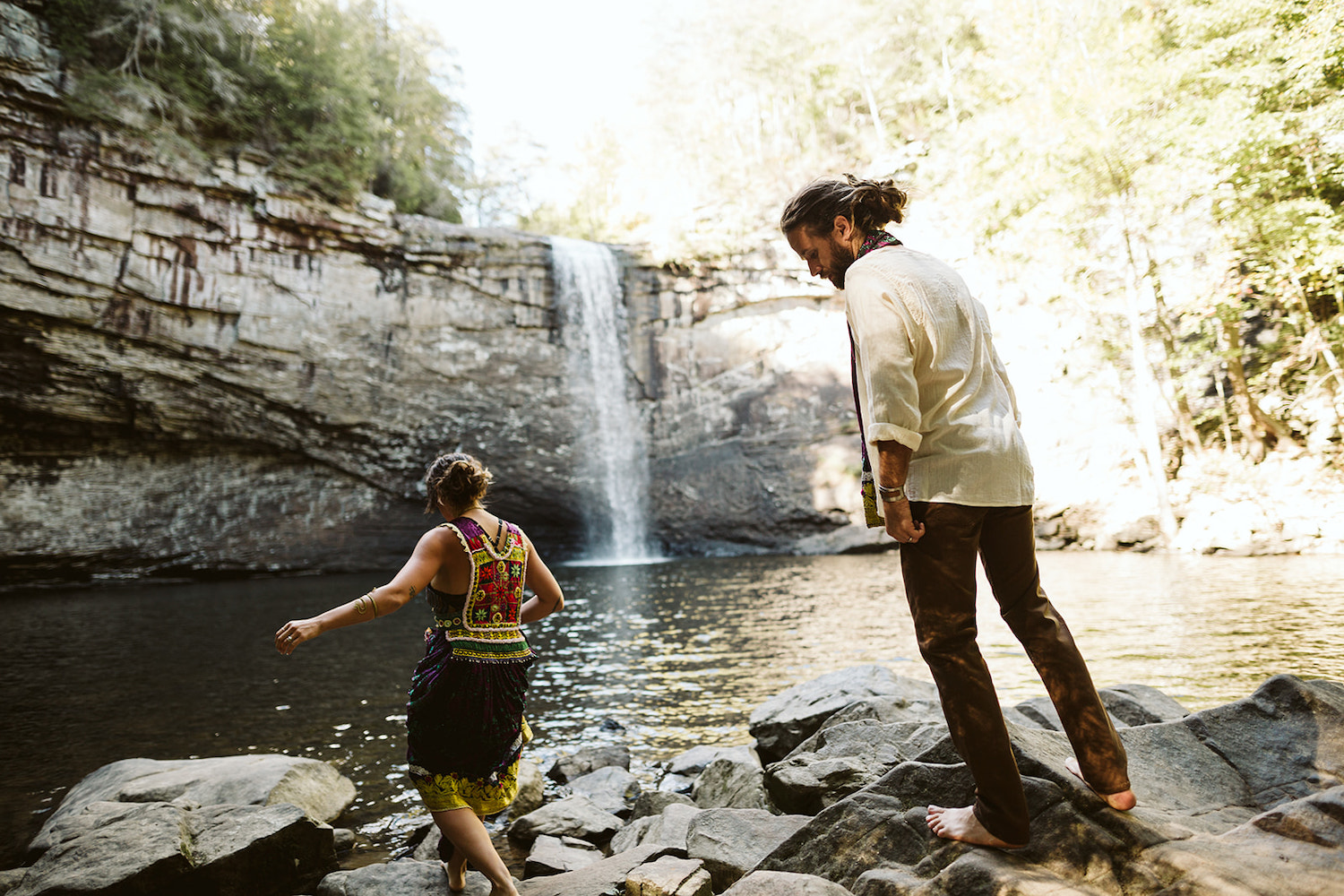 man and woman dressed in Bohemian style climb barefoot over rocks at Chattanooga's Foster Falls for wedding portraits