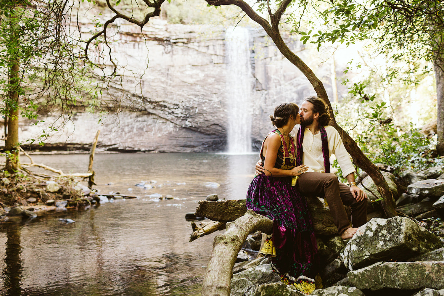 man and woman in colorful Bohemian style dress kiss while sitting on a tree branch at Foster Falls near Chattanooga