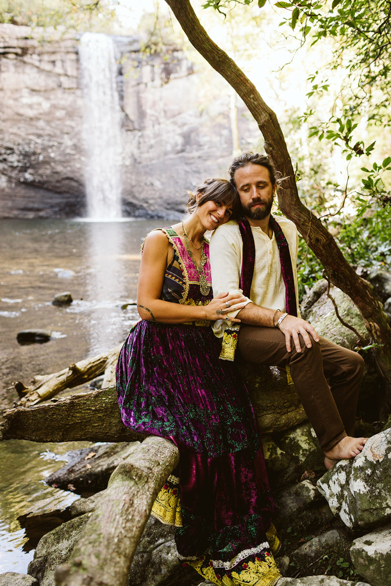 man and woman in colorful Bohemian style dress snuggle while sitting on a tree branch at Foster Falls near Chattanooga