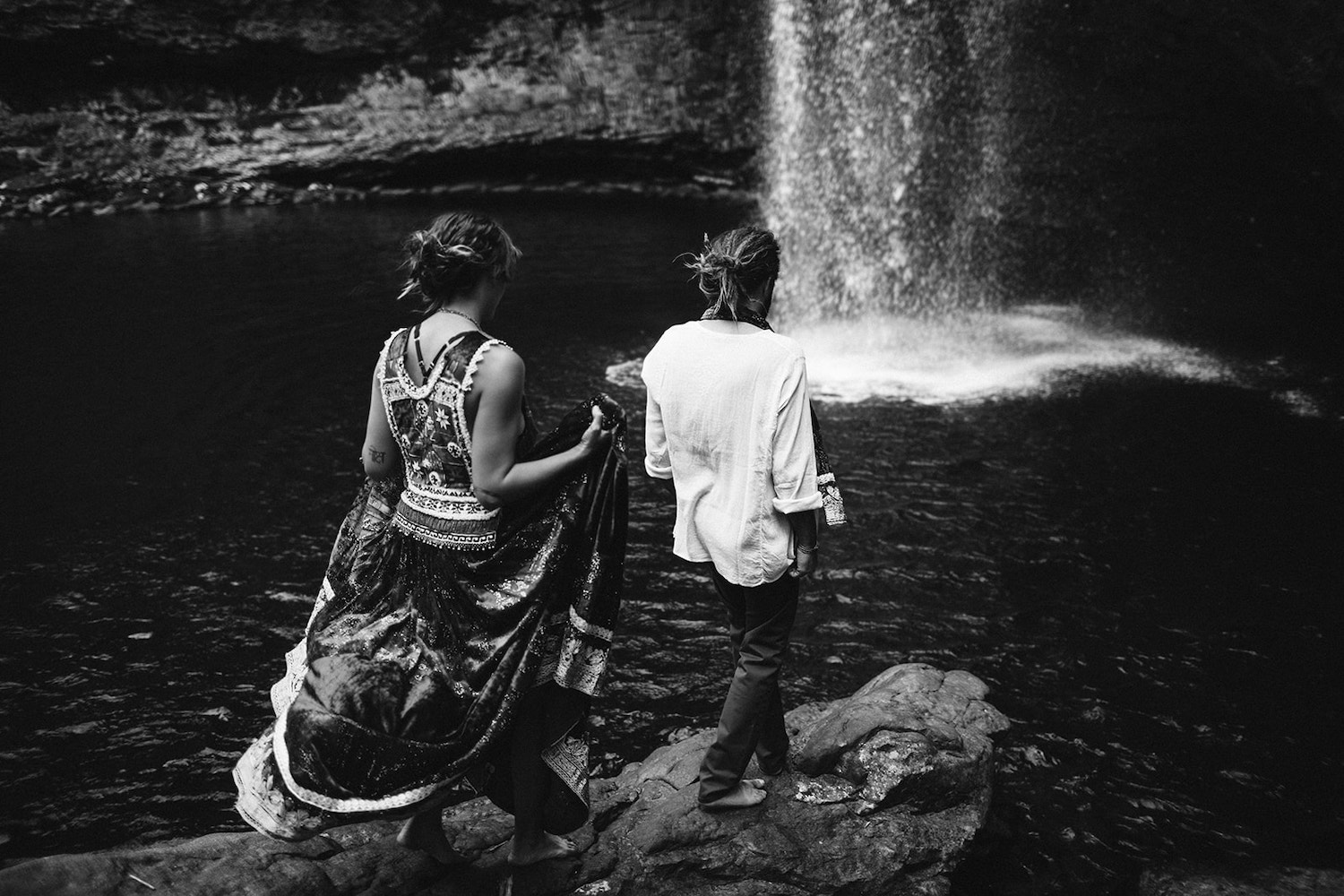man and woman dressed in Bohemian style climb barefoot over rocks at Chattanooga's Foster Falls for wedding portraits