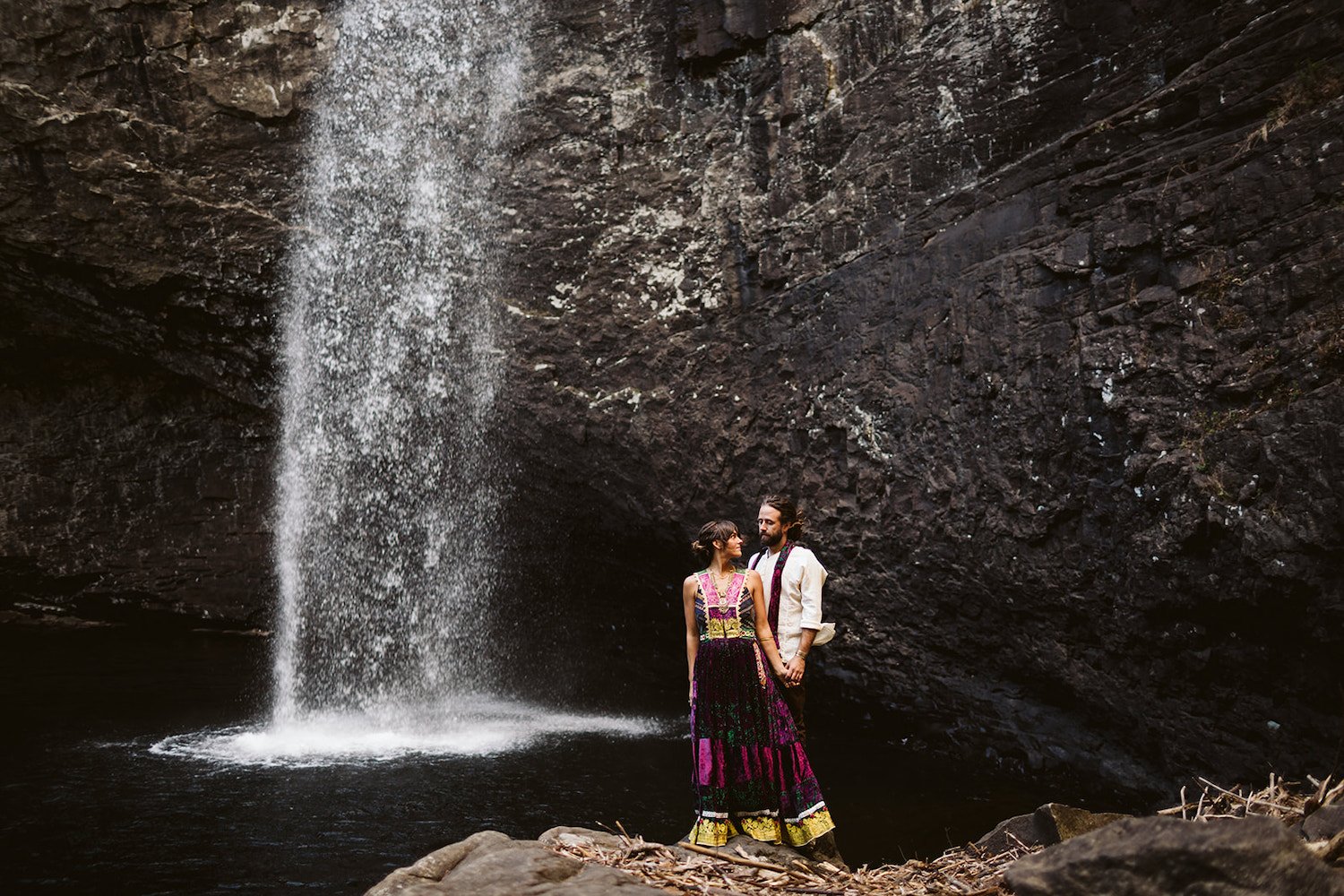 man and woman dressed in Bohemian style dress stand on rocks next to Chattanooga's Foster Falls for wedding portraits