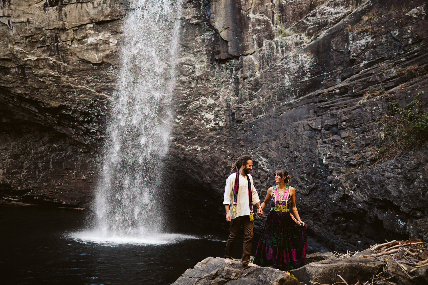 man and woman dressed in Bohemian style climb barefoot over rocks at Chattanooga's Foster Falls for wedding portraits